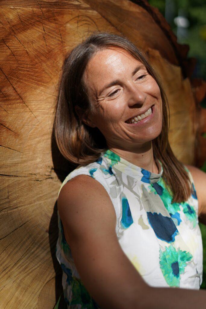 Verena lehnt an einem Baum und genießt die Sonne – Symbol für innere Ruhe & Lebensenergie